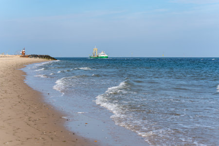 Beach with waves and a ship. A sandy beach with gentle waves meets the blue sea. A green ship sails...