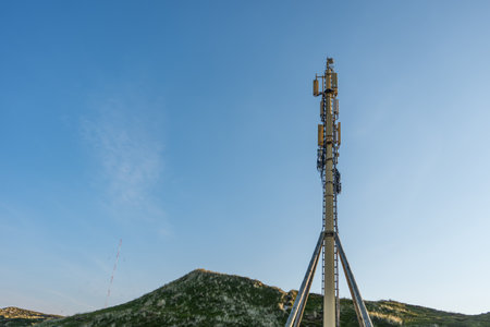 Communication Tower in the Dunes. A tall cell tower rises above grassy dunes under a clear blue sky....