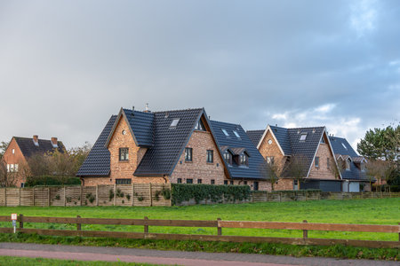 Residential brick houses with dark roofs. Modern brick houses with steep dark roofs in a quiet suburban neighborhood. The view shows fenced gardens and green lawns under a cloudy sky.の写真素材