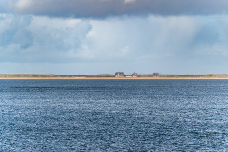Horizon over calm sea. Distant houses on the coastline under dramatic clouds. Calm blue water stretches across the frame.の写真素材