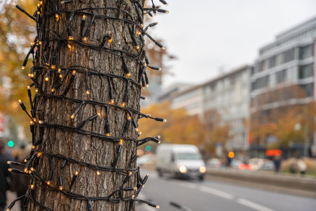 Tree wrapped in warm fairy lights beside a busy boulevard. Soft bokeh city traffic fades in the background.の写真素材