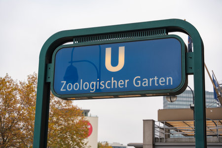 Classic blue U-Bahn sign marks station Zoologischer Garten. Foliage and city forms blur in the...