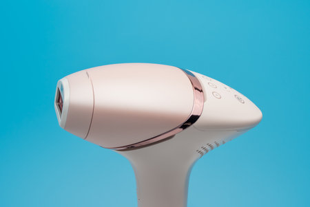Close-up of IPL hair removal handset in rose gold on blue background. Studio shot highlights design details and control buttons.の写真素材