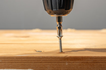 Screw being driven into a wooden board by a drill bit in a tight close-up. Hands-free fastening concept with clean background blur.の写真素材