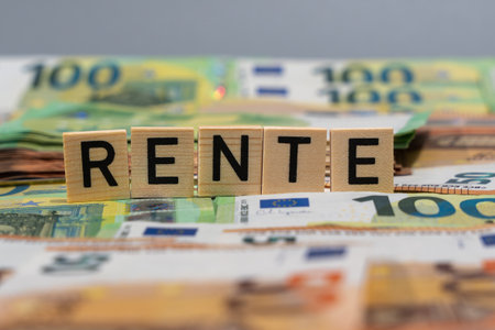 Close-up of wooden tiles reading Rente on euro cash. Blurred banknotes in the background suggest pension payments, savings, and retirement security.の写真素材