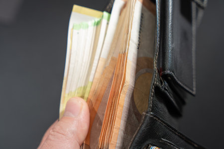 Hand holds an open black leather wallet packed with euro banknotes. Close-up view suggests cash payment, budgeting, and financial security.の写真素材