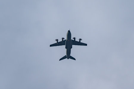 Four-engine turboprop transport aircraft seen from below against a pale sky. Clean silhouette with...