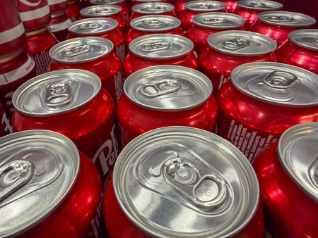 Germany Berlin February 7, 2026. Macro close-up of aluminum soda can lids on red soft drink cans. Industrial beverage packaging texture emphasizing repetition and material detail.のeditorial素材