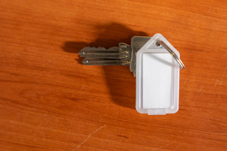 A key is on a wooden surface. The key is silver and has a white tag on it