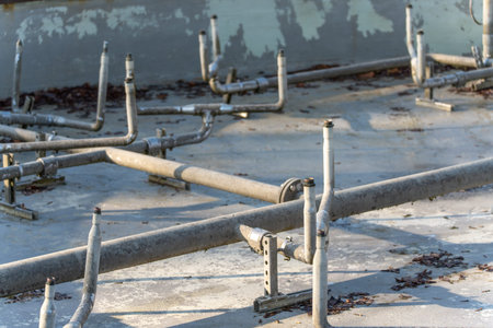 Industrial metal pipe system installed on a concrete basin floor. Weathered steel tubes and valves...