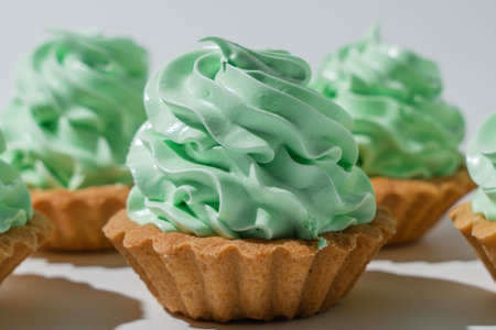 A small pastry tart topped with a glossy mint green cream swirl. The dessert sits on a clean white...