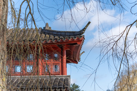 Traditional Chinese pavilion with red pillars and curved eaves. Bare tree branches frame the...