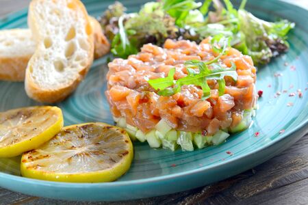 fresh salmon tartare garnished with arugula, toasted toast and two slices of lemon on a blue plate.の写真素材