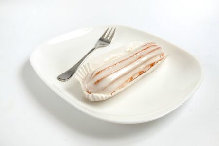eclair and fork on a white plate on a white background.の写真素材