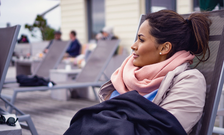 Young woman relaxing at a cafe with a wool blanket and a scarf on.の写真素材