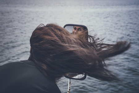 Young female model looking in a mirror with heavy wind going through her hair .の写真素材