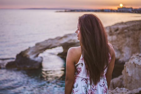 Beautiful dark skinned woman posing in front the Love Rock in Cyprus, Greece while watching the sunset.の写真素材