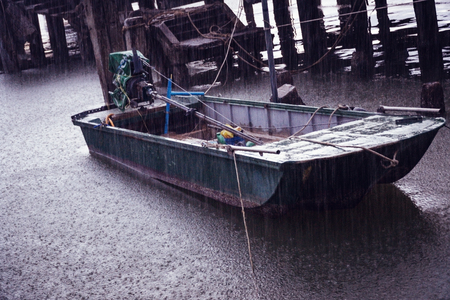 Old single motor boat in heavy rain at a port in Thailand.の写真素材