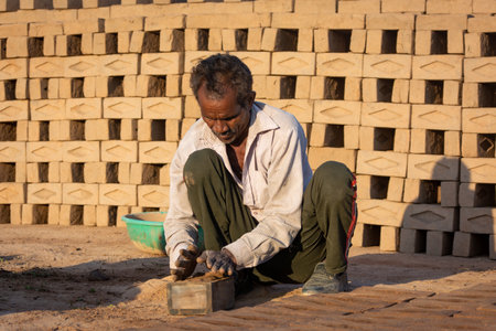 TIKAMGARH, MADHYA PRADESH, INDIA - AUGUST 11, 2021: Indian man making house bricks by hand using a mold and wet clay.のeditorial素材