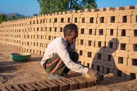 TIKAMGARH, MADHYA PRADESH, INDIA - AUGUST 11, 2021: Indian man making house bricks by hand using a mold and wet clay.のeditorial素材