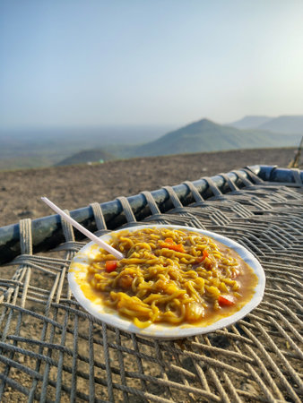 A bowl of steaming Noodles rests on a disposable plate with a vast hazy landscape and distant mountain peaks in the backgroundの写真素材