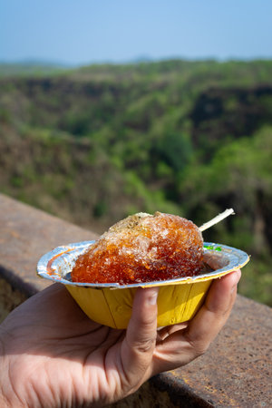 Hand holding a traditional Indian khatta gola against a scenic natural backdrop. A refreshing summer treat.の写真素材