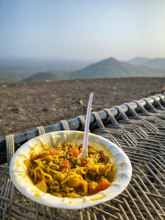 A bowl of steaming Noodles rests on a disposable plate with a vast hazy landscape and distant mountain peaks in the backgroundの写真素材