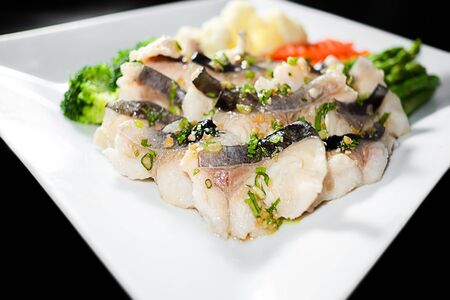 Slice steamed fish with braised leeks topping and spicy sauce in black background