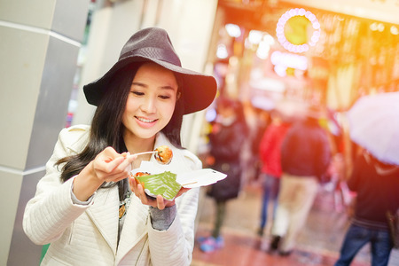 Chinese Asian young female model eating dumpling batter (Takoyaki) on Street in Hong Kongの写真素材