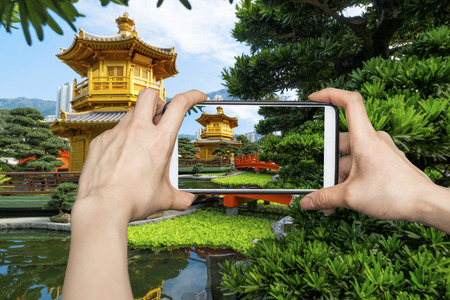Girl taking pictures on mobile smart phone in Front View The Golden Pavilion Temple in Nan Lian Gardenの写真素材