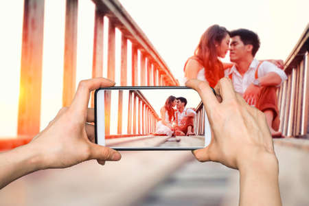 Girl taking pictures on mobile smart phone Happy couple relaxing in sunsetの写真素材