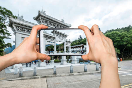 Girl taking pictures on mobile smart phone in Front View of Tian Tan Giant Buddha in blue skyの写真素材