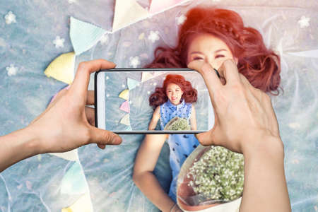 Girl taking pictures on mobile smart phone a beautiful young girl with a bouquet of flowersの写真素材