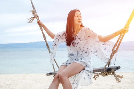 Beautiful woman sitting on a swing on the beach  in Koh Phangan, Thailandの写真素材