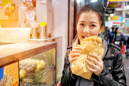 Young woman eating waffle street food in hong kongの写真素材