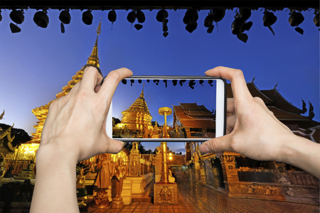 Woman Taking pictures on mobile smart phone showing Night view of Wat Phra That Doi Suthep, Chiang Mai, Popular historical temple in Thailand.の写真素材