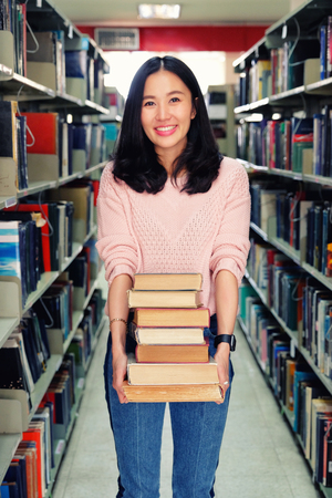 Young woman carrying heavy books in library