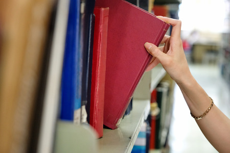 Young woman picking a book off the shelf in a libraryの写真素材