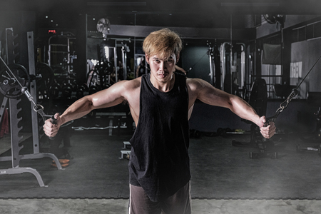Strong fitness man doing arm workout with cable machine in the gymの写真素材