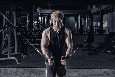 Strong fitness man doing arm workout with cable machine in the gymの写真素材