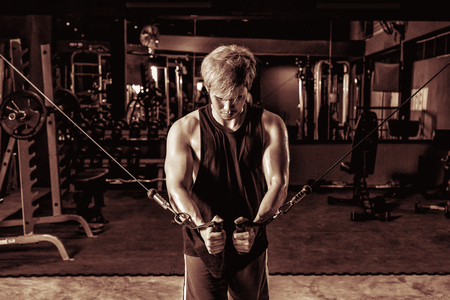 Strong fitness man doing arm workout with cable machine in the gymの写真素材
