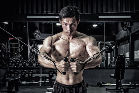 Strong fitness man doing arm workout with cable machine in the gymの写真素材