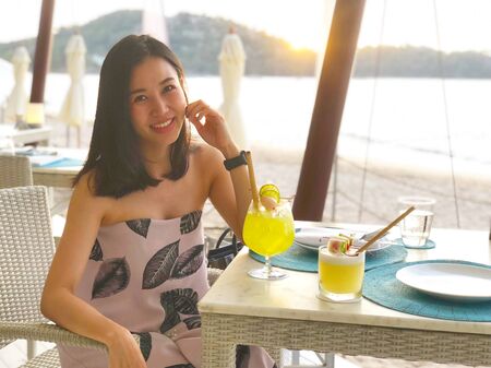 Beautiful woman holding a fruit cocktail on a tropical beach at sunsetの写真素材