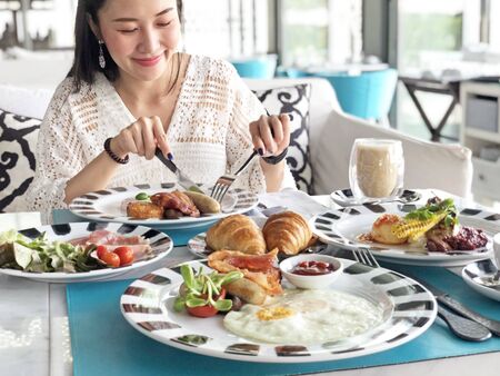 Young woman having healthy breakfast - fried egg, beans, salad, tomatoes, mushrooms, bacon and toast.の写真素材
