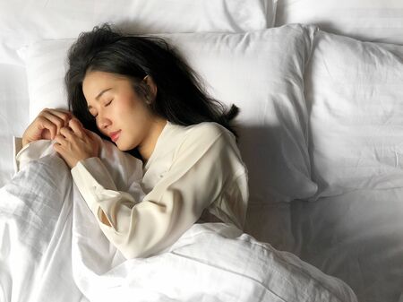 Beautiful asian woman sleeping in bed under white quilt with head on pillow comfortable and happy. girl with relax for health concept.の写真素材