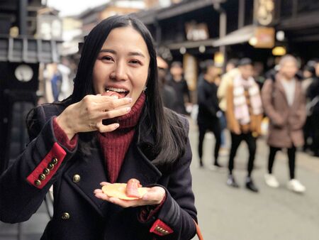 Young woman tourist enjoy eating Japanese street food Hida Beef Sushi and cracker at Takayama, Japanの写真素材