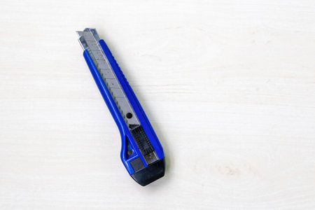 Blue color anti-cutter on light white wooden background. A pointed, sharp-edged knife cutter.