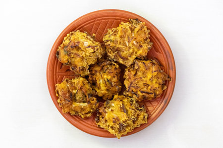 Crispy pakora on a clay plate, isolated on a white background. These delicious, deep-fried fritters are a popular snack or appetizer in Bangladesh, India, and other parts of South Asia. Top view.の写真素材