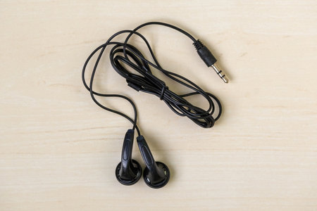 Black wired earphones on a wooden background, top view.