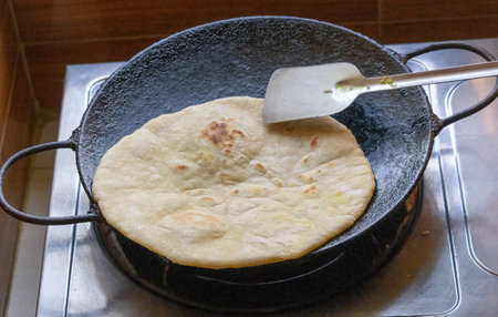 Close-up of homemade bread cooking in an iron tawa, stirred with a steel spatula.の写真素材